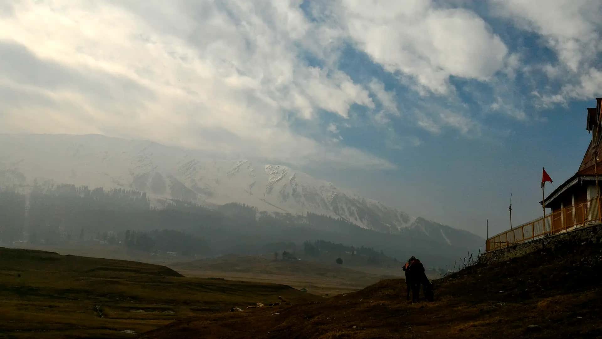 Snow-covered Pir Panjal peaks above the brown Gulmarg meadow in late November, with a horse grazing on the slope